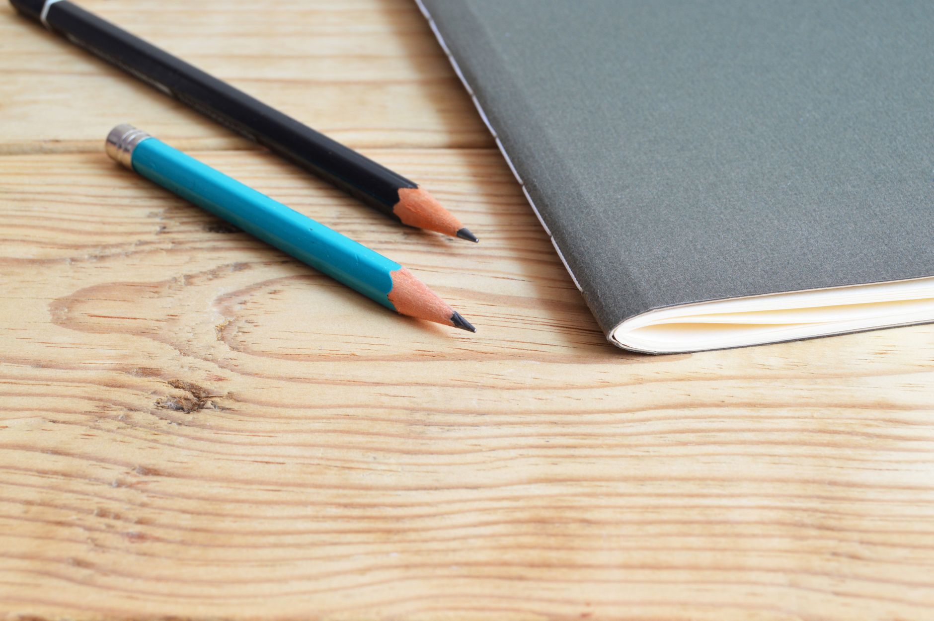 A notebook and pencils on a wooden desk. Photograph by ClickerHappy, via Pexels.