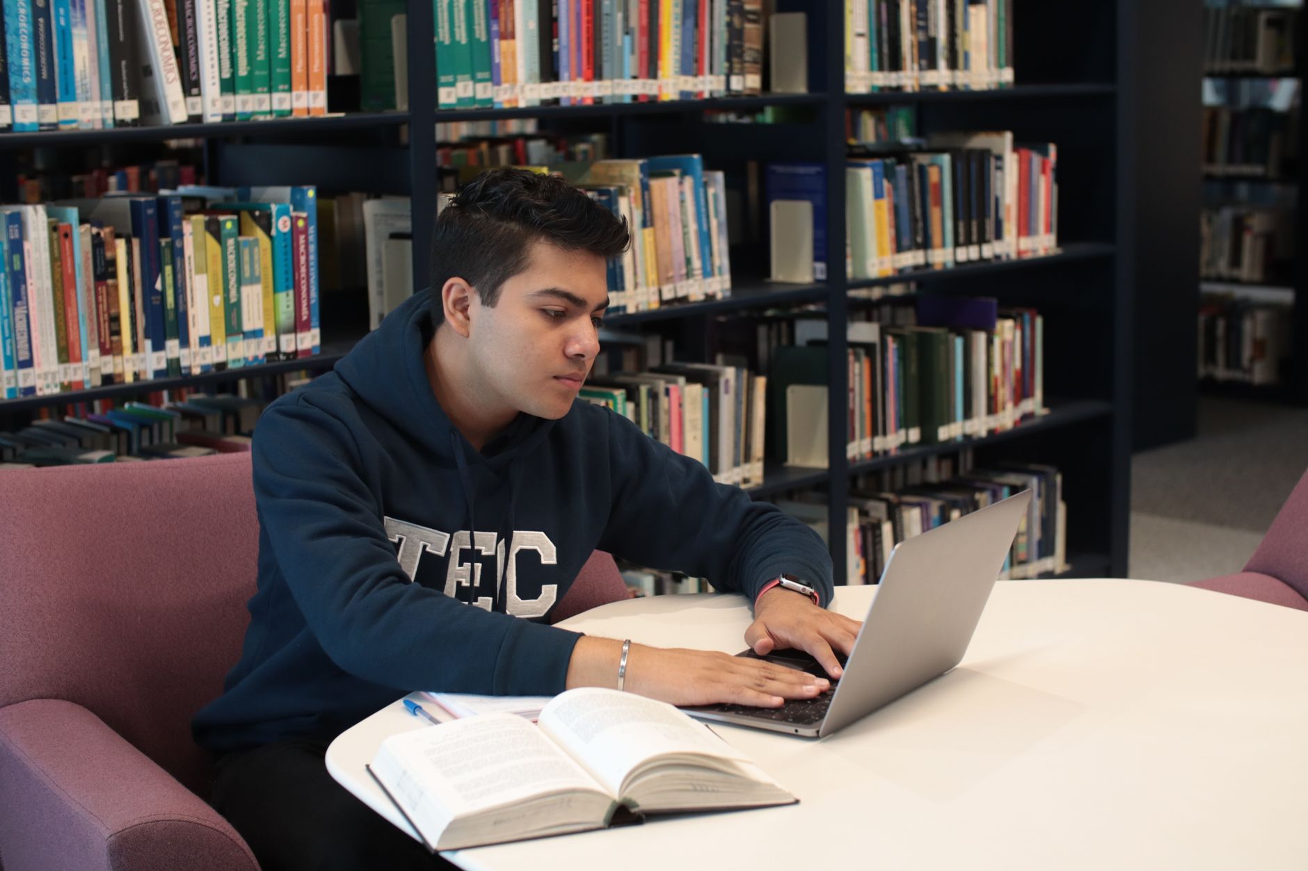 A student studying with a laptop and books in a library. Photograph by Ludovic Delot, via Pexels.